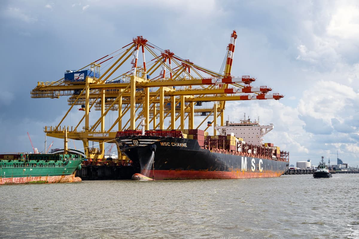 a massive yellow crane lifting a shipping container shaped like a luxury stadium suite