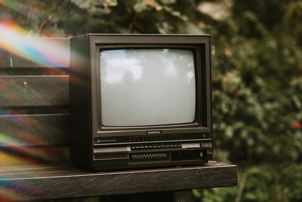 a dusty vintage television set sitting alone in a lush green forest