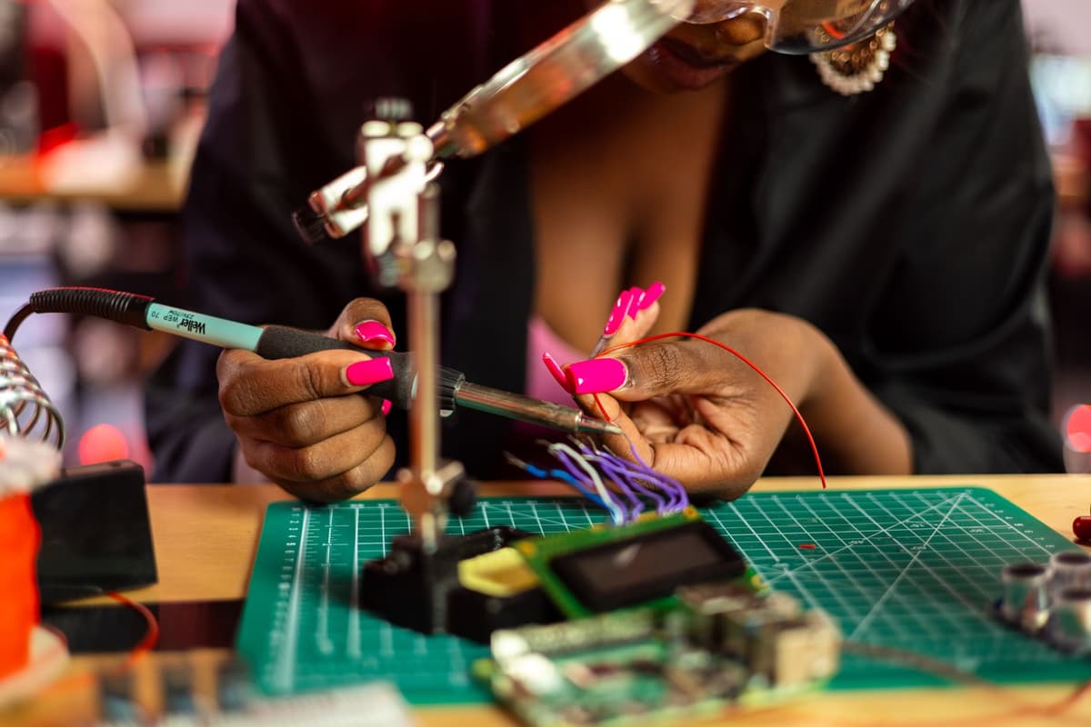 a weathered hand soldering a small green circuit board