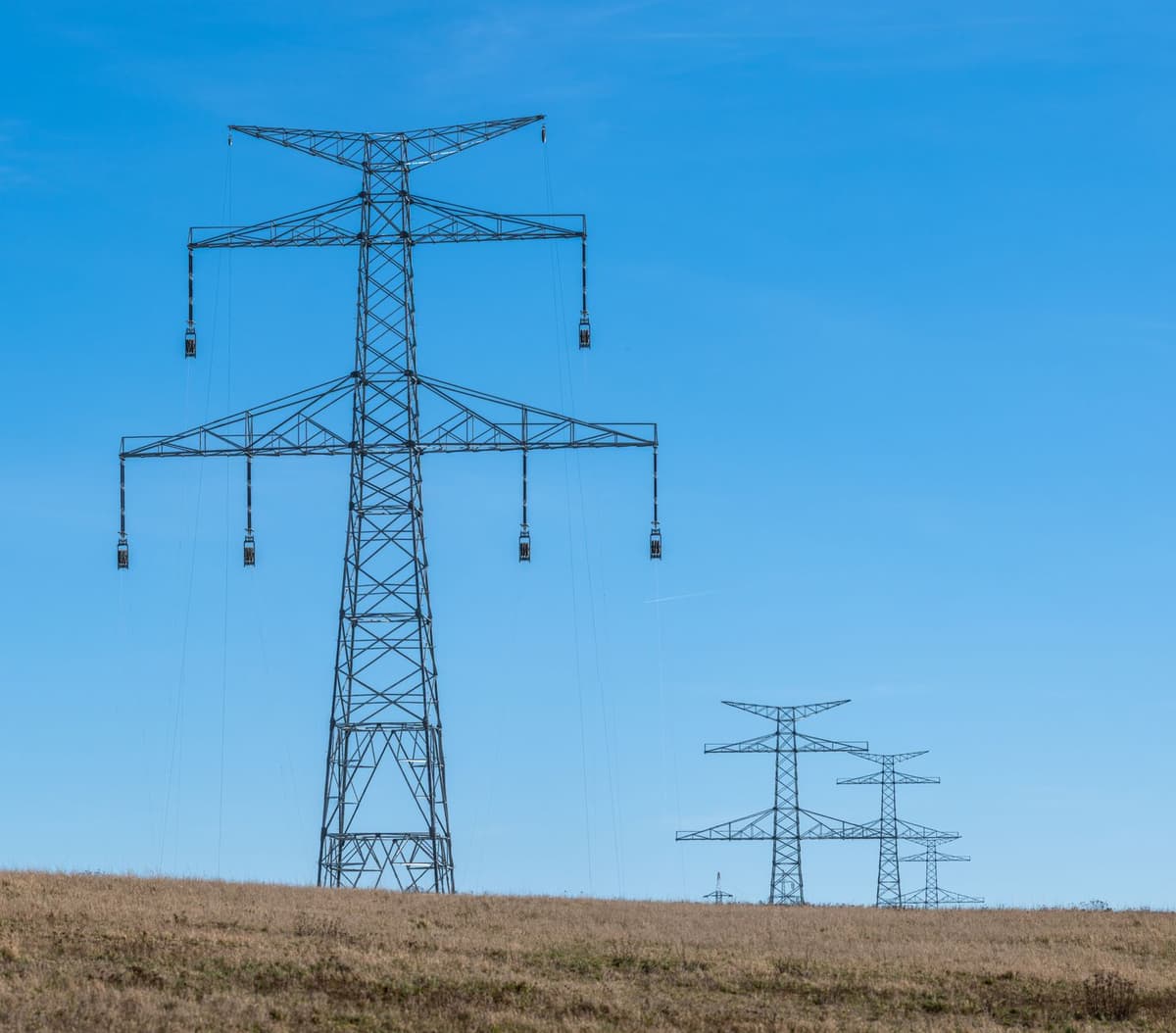 a single massive metal transmission tower rising out of a muddy cornfield under grey skies