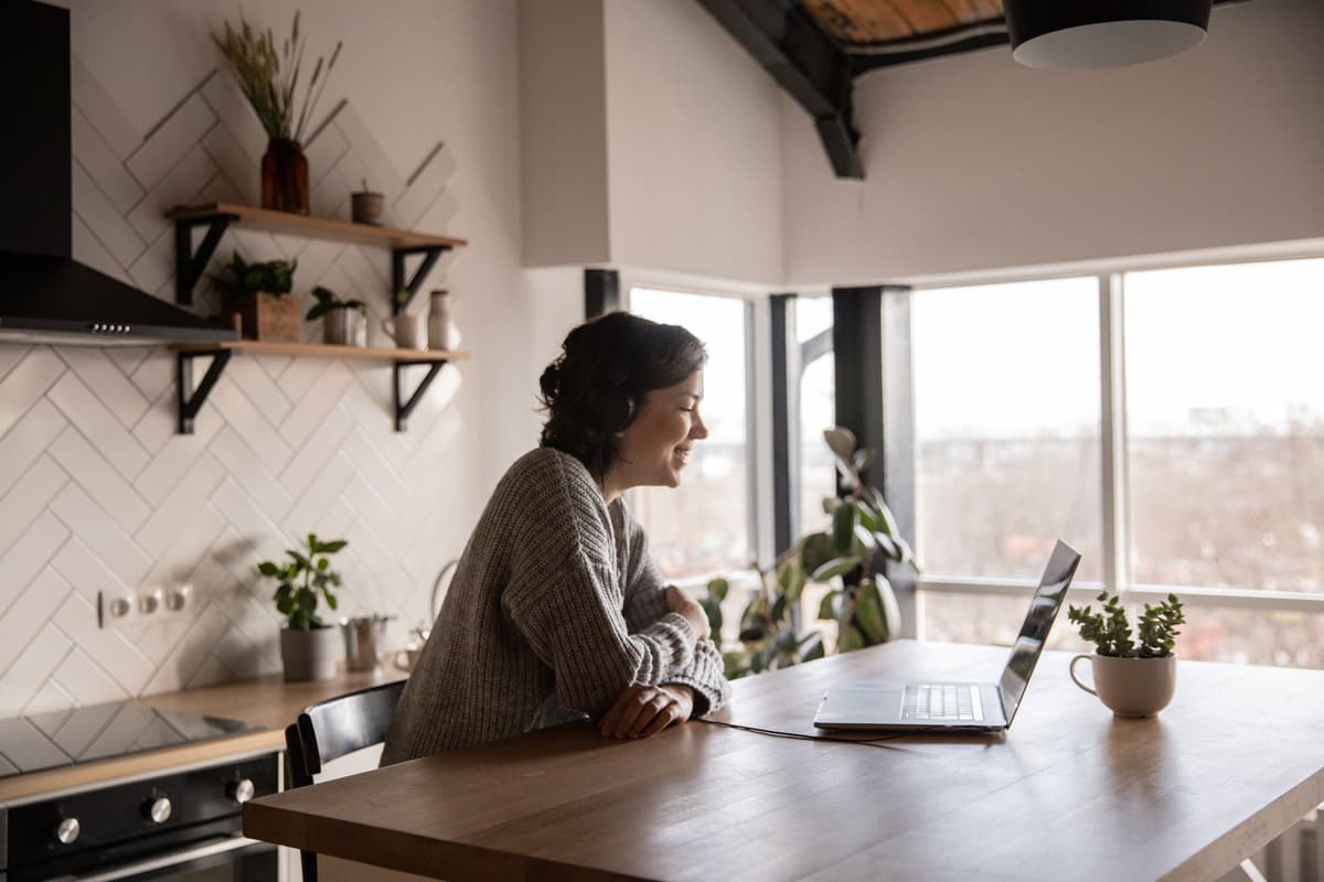 a hooded figure using a laptop in a bright modern kitchen