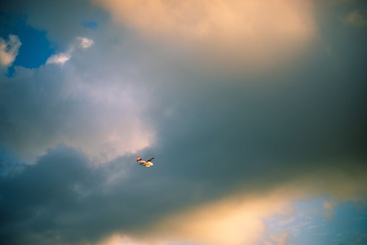 a single white firefighting plane dwarfed by a massive dark gray cloud tower