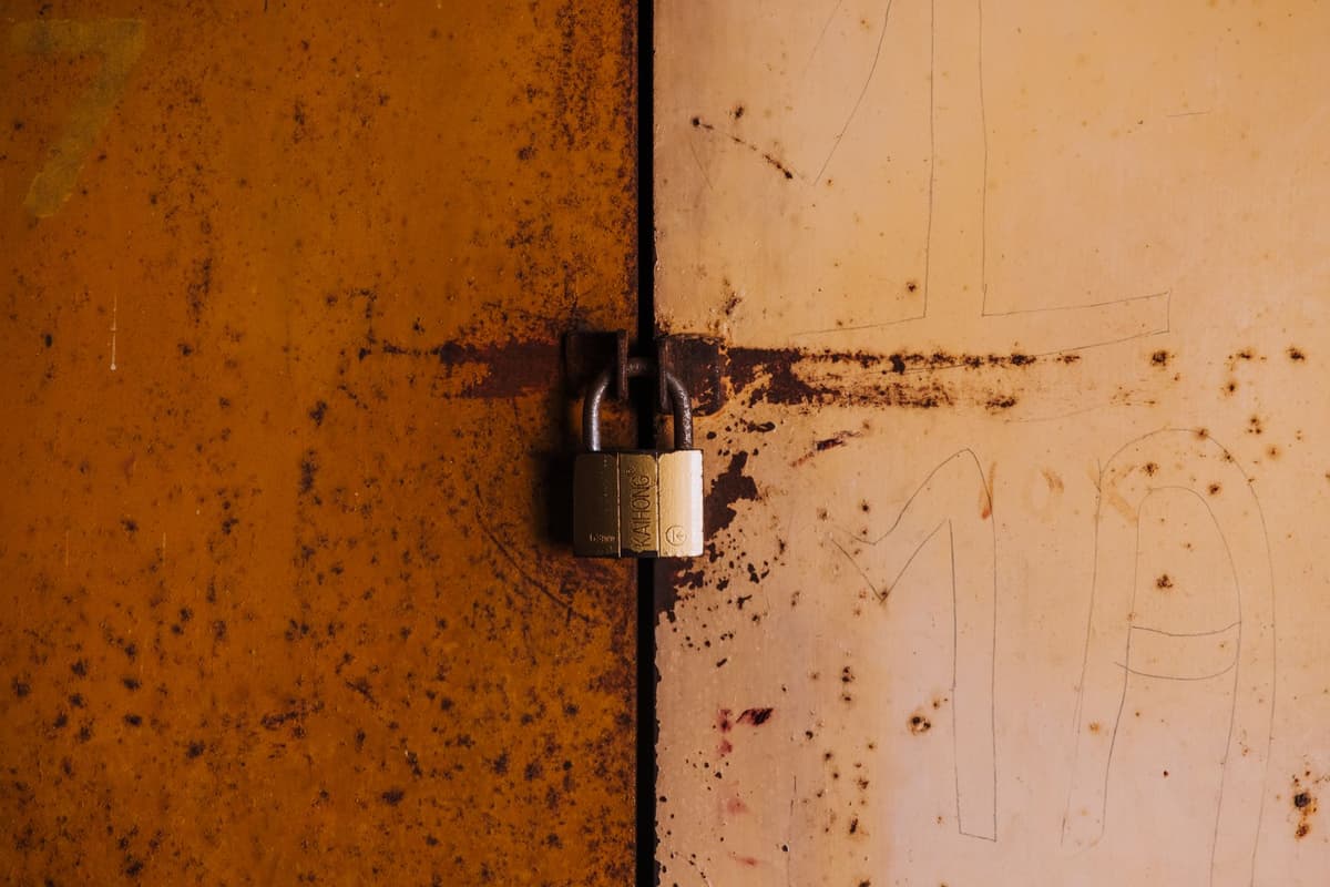 a rusted, weed-choked stadium gate with a padlock