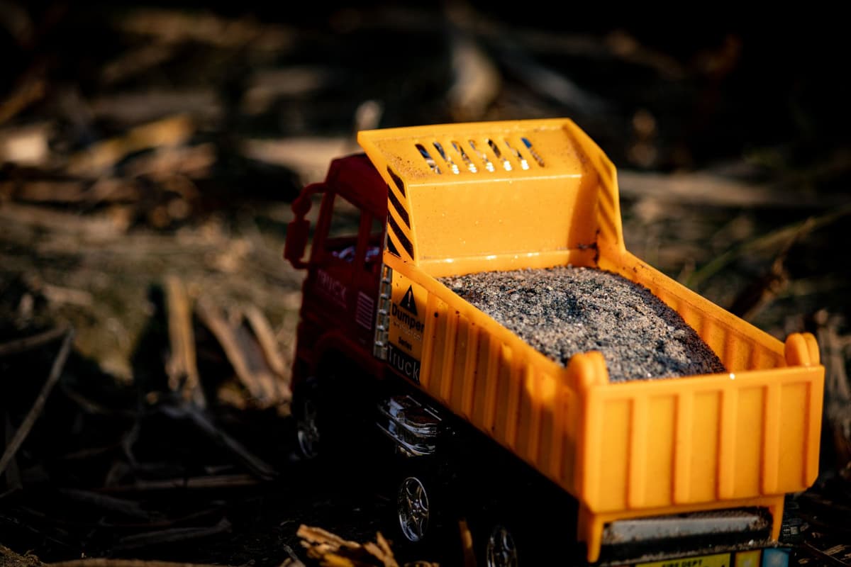 a massive yellow dump truck carrying one tiny pebble