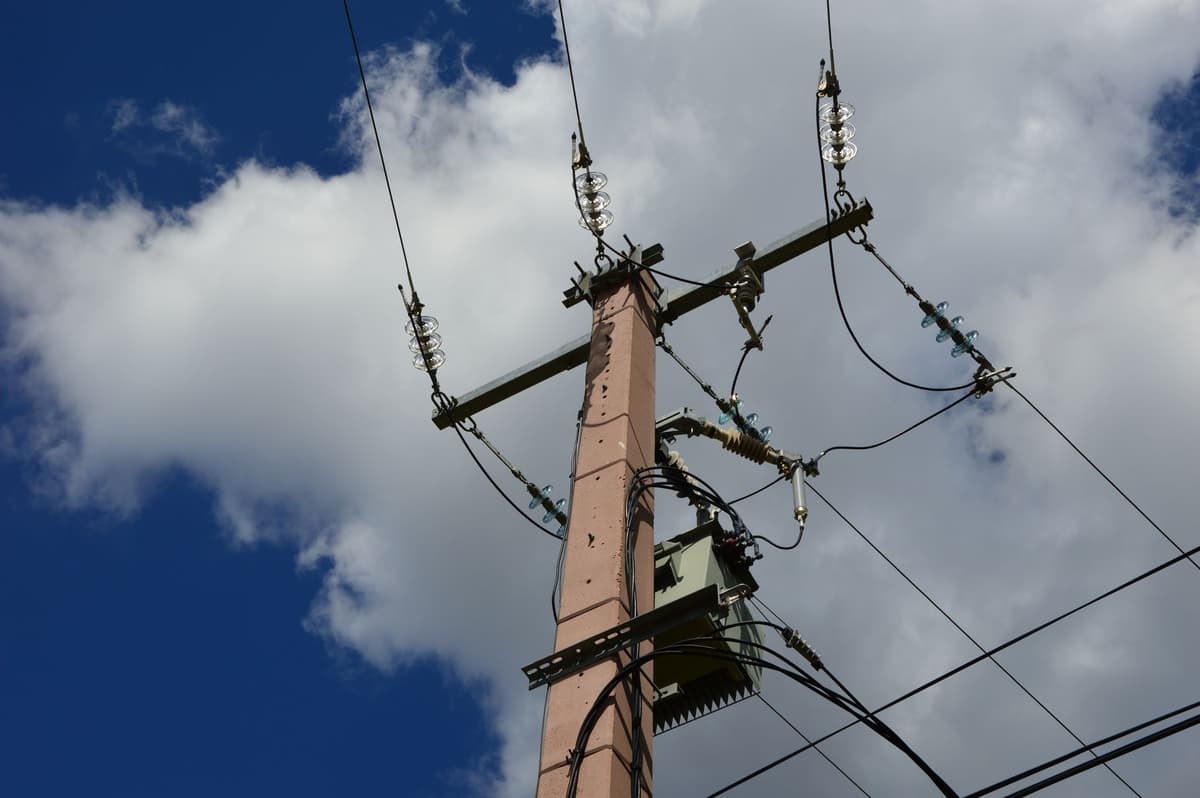 a broken camera pole with wires dangling against a cloudy sky