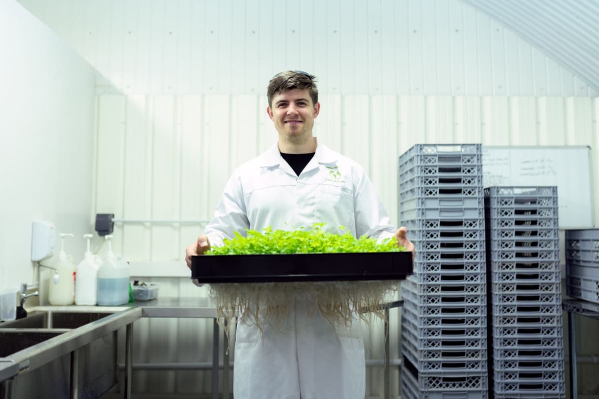 a scientist in a mud-stained vest holding a tiny weed like a trophy