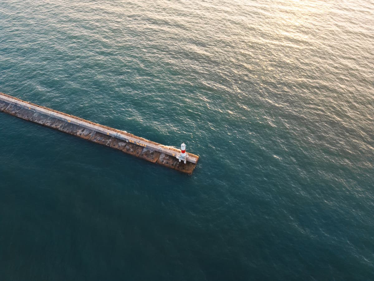 a giant metal beacon reflecting sunlight near a harbor