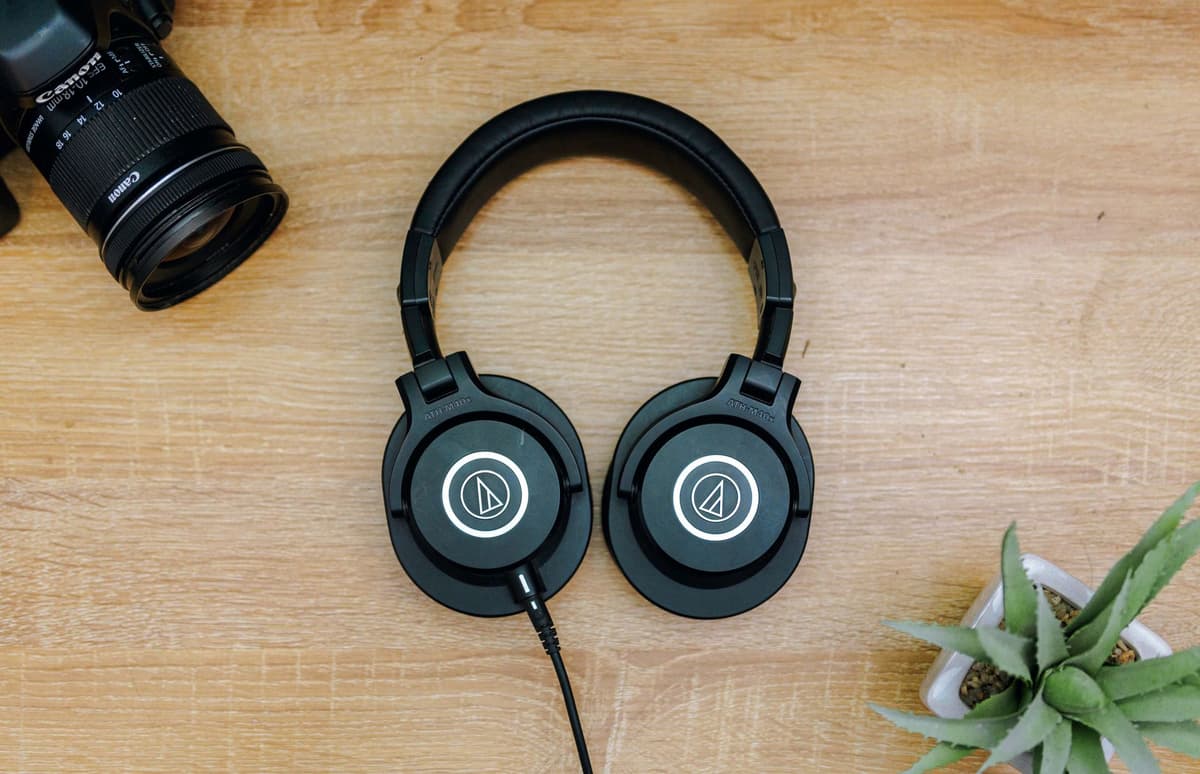 a high-end smartphone lying on a wooden desk next to professional studio headphones