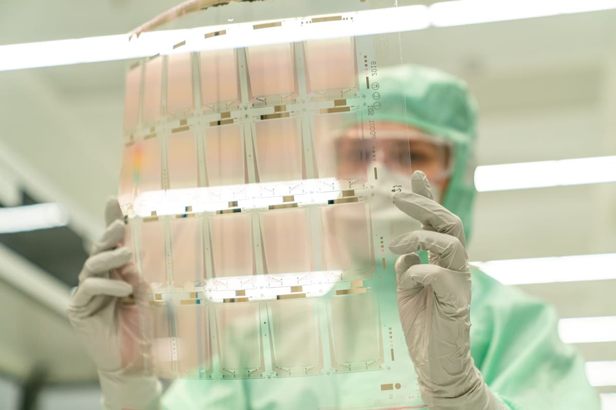 a giant silicon wafer held by a person wearing white cleanroom gloves