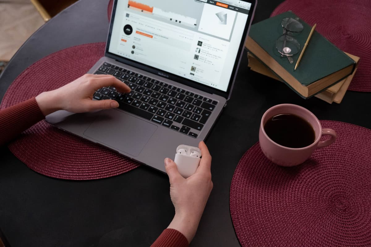 a person holding disconnected wireless headphones near a laptop