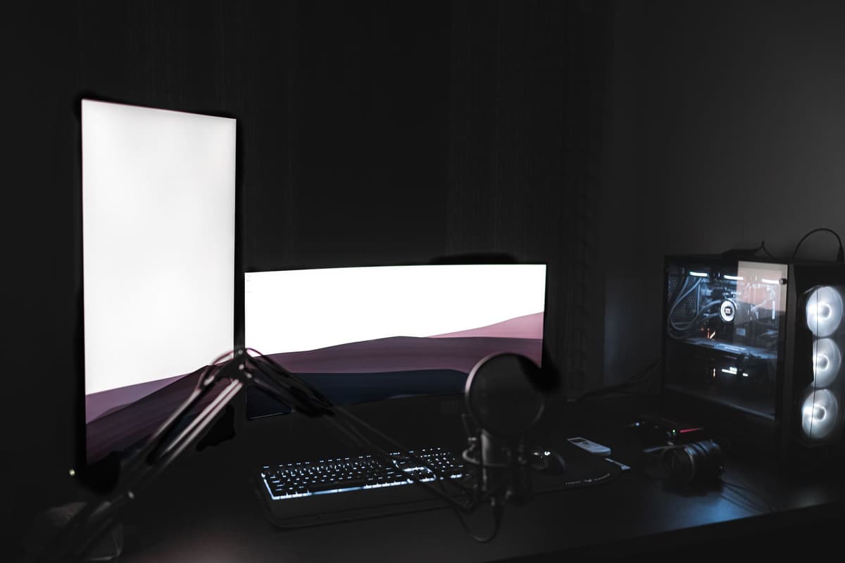 a single lit desk lamp in a dark room reflecting on a dusty monitor
