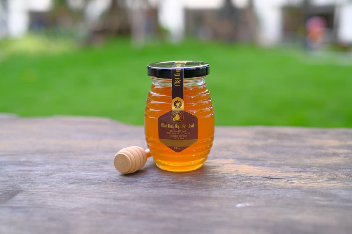 a small ornate glass jar with golden honey spilled on a marble countertop