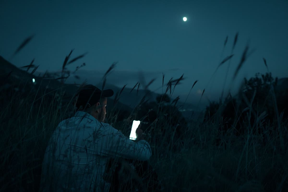 a person sitting alone in a dark room illuminated by a glowing smartphone screen