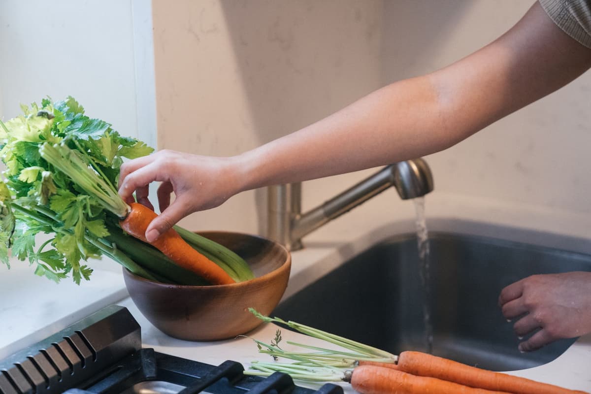 a hand covered in dark mud holding a bright orange carrot