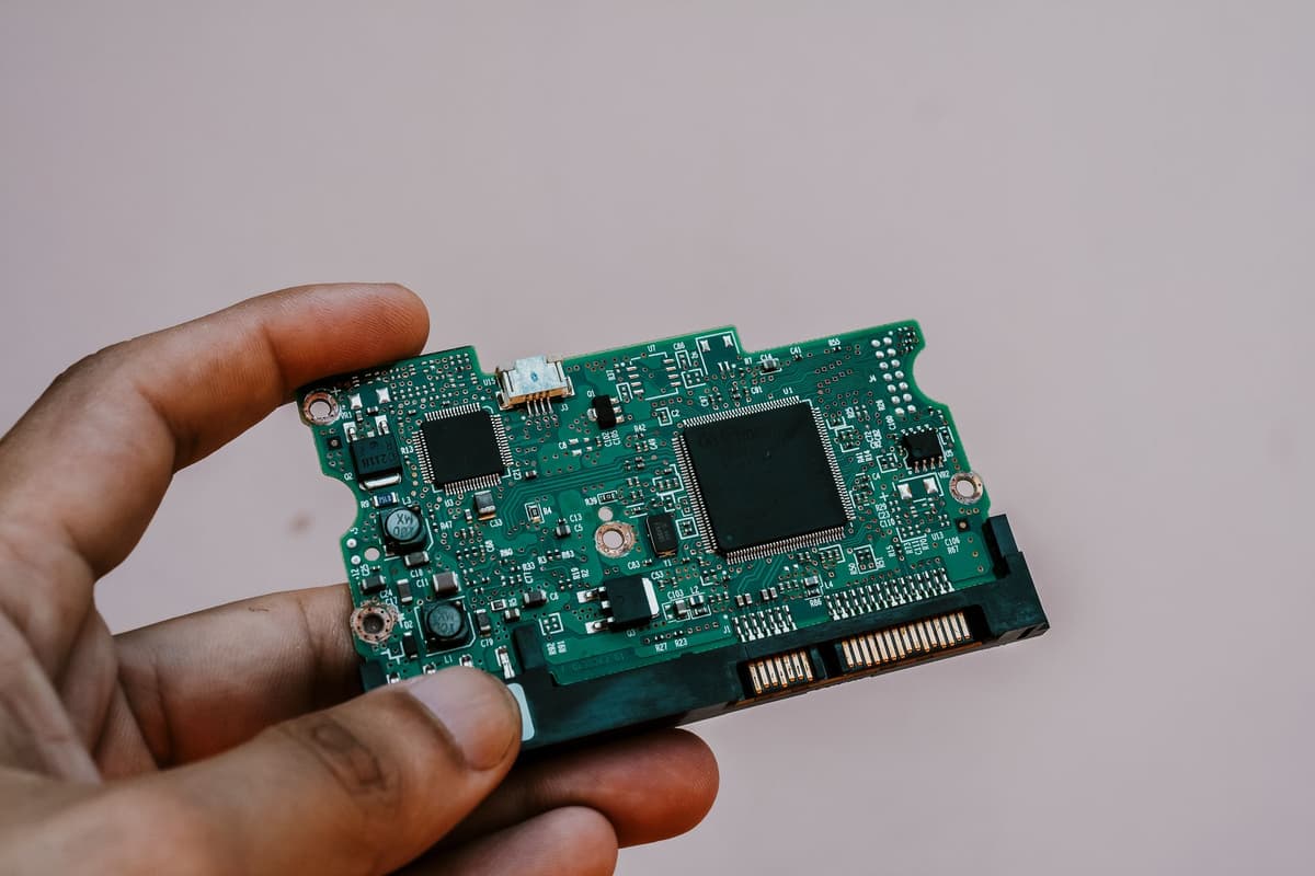 a single green circuit board on a cluttered wooden desk
