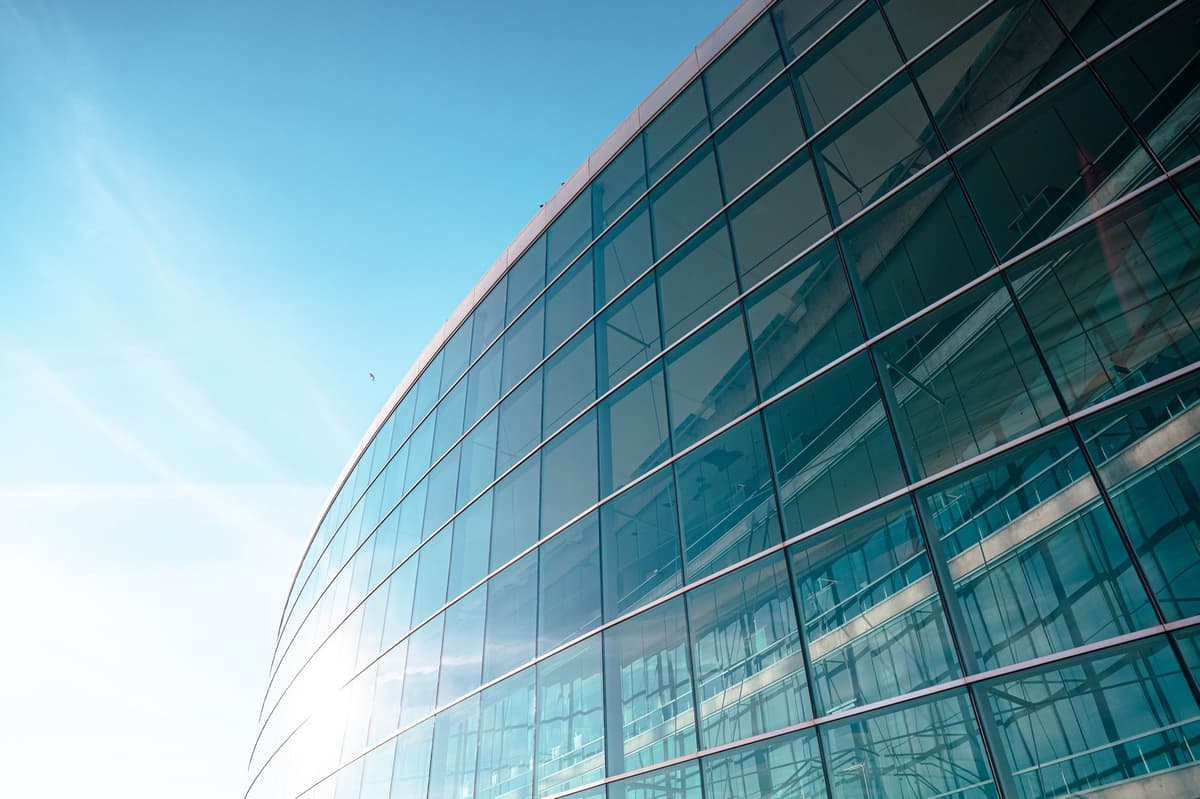 a modern glass office building reflecting a clear blue sky