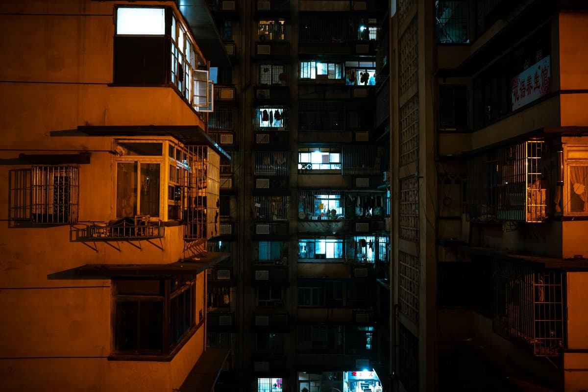 a single glowing window in a dark brutalist apartment complex