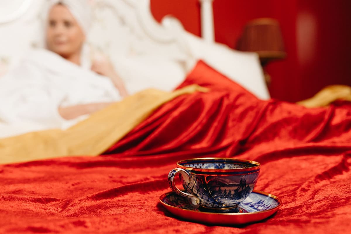 a Victorian-style bedroom with a plastic skeleton sitting in a rocking chair holding a tea cup