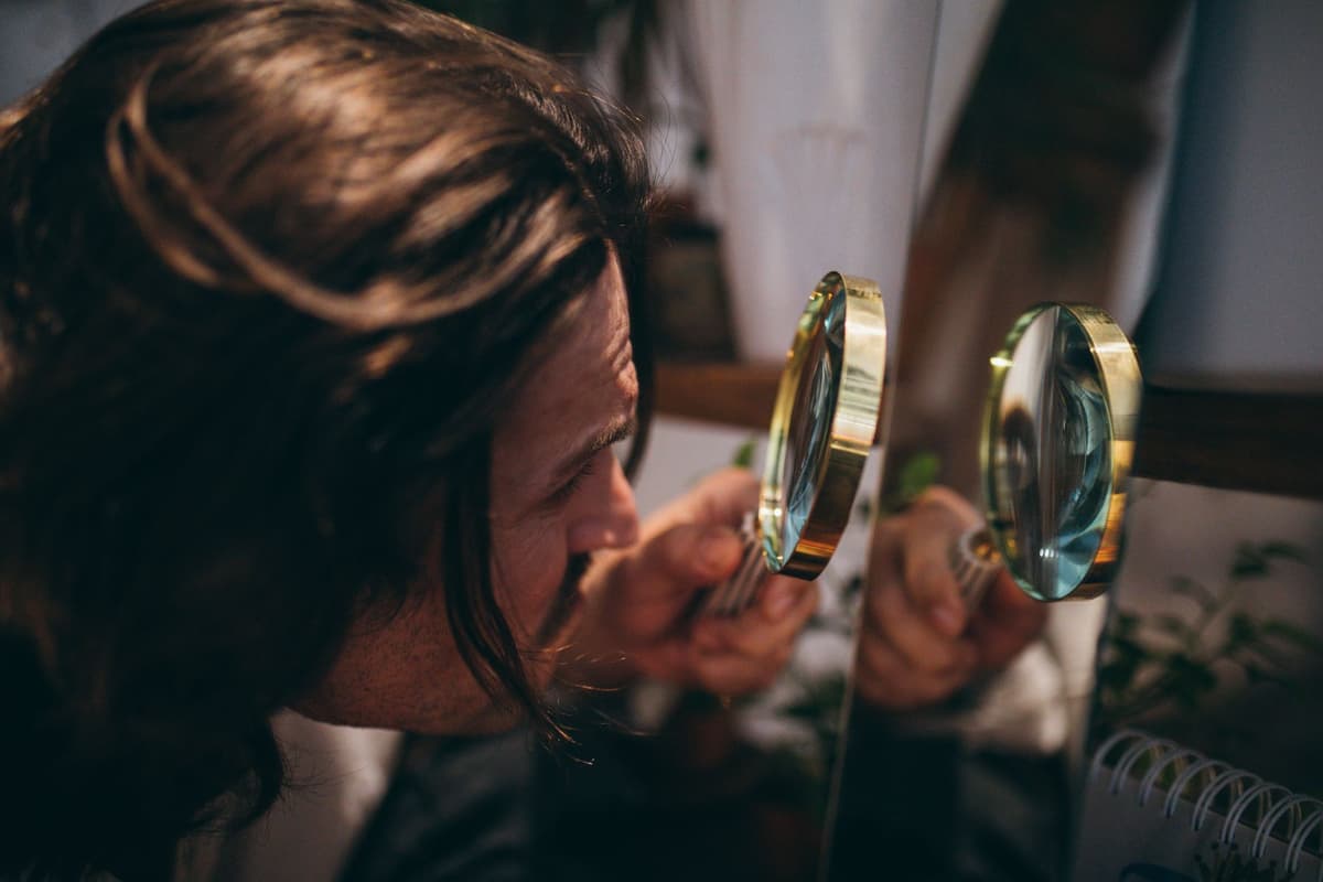 a person holding a magnifying glass to a smartphone screen, looking for a watermark