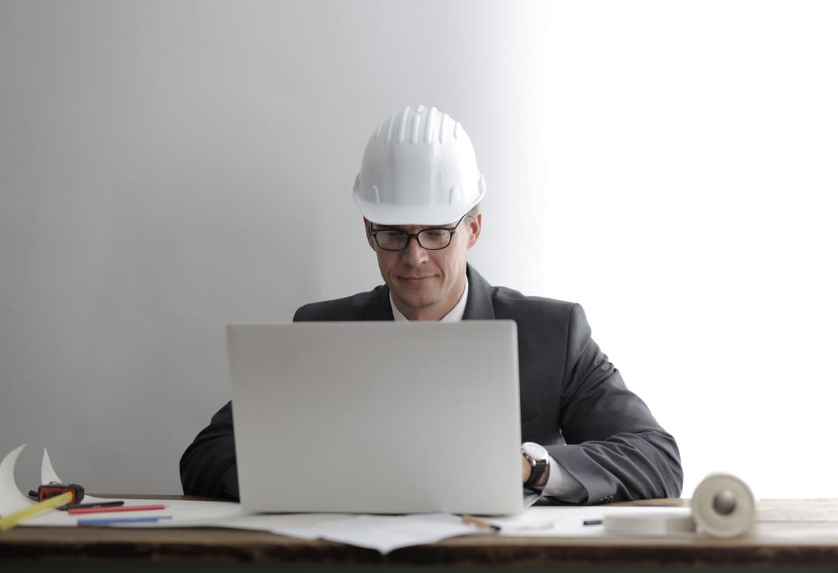 a man in a hard hat holding a laptop while staring at a massive hole in the street