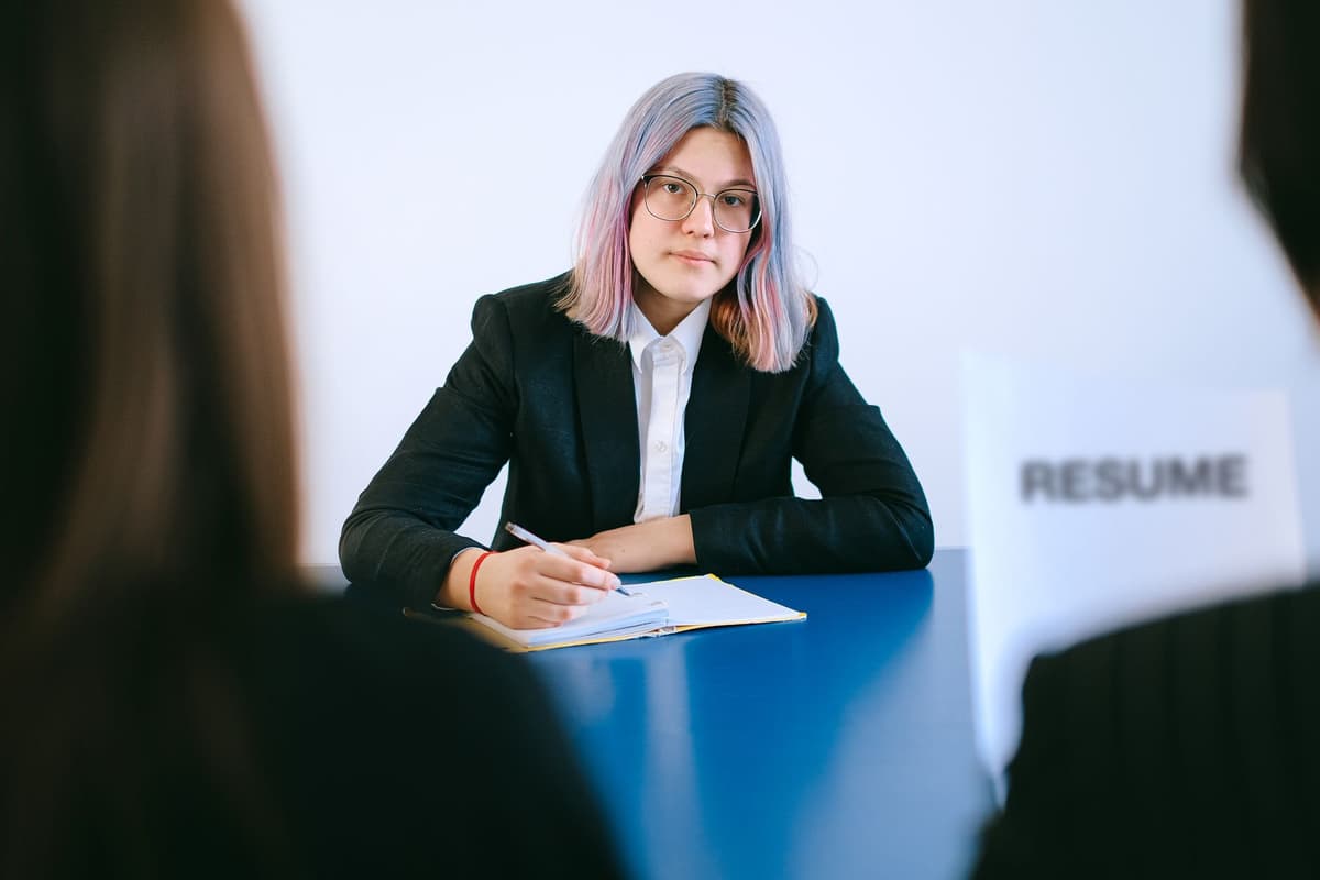 a person sitting across a wooden desk looking intently at a recruiter taking notes