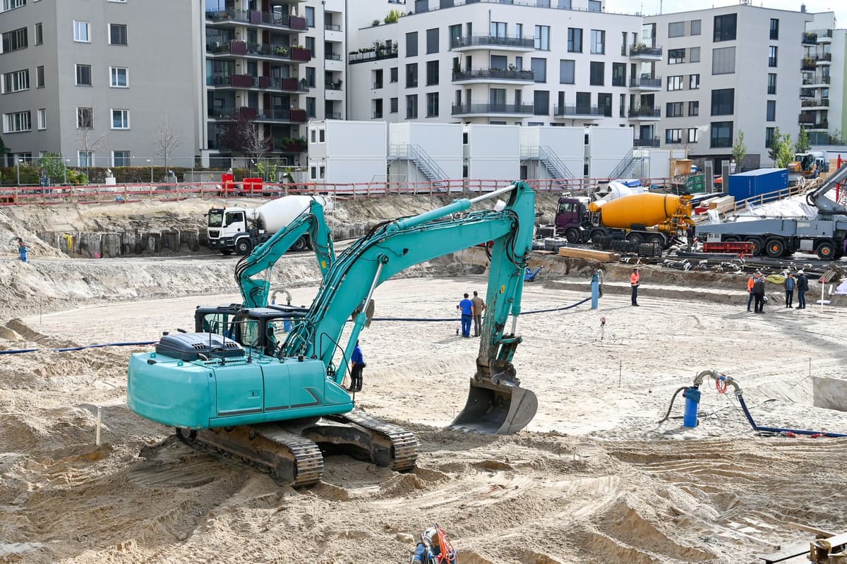 a massive yellow excavator bucket resting near a tiny safety cone