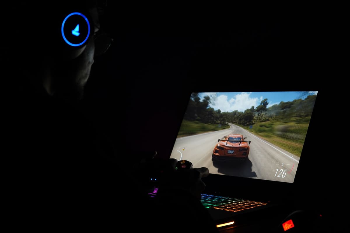 a man in a headset hunched over a glowing laptop screen in a dark room