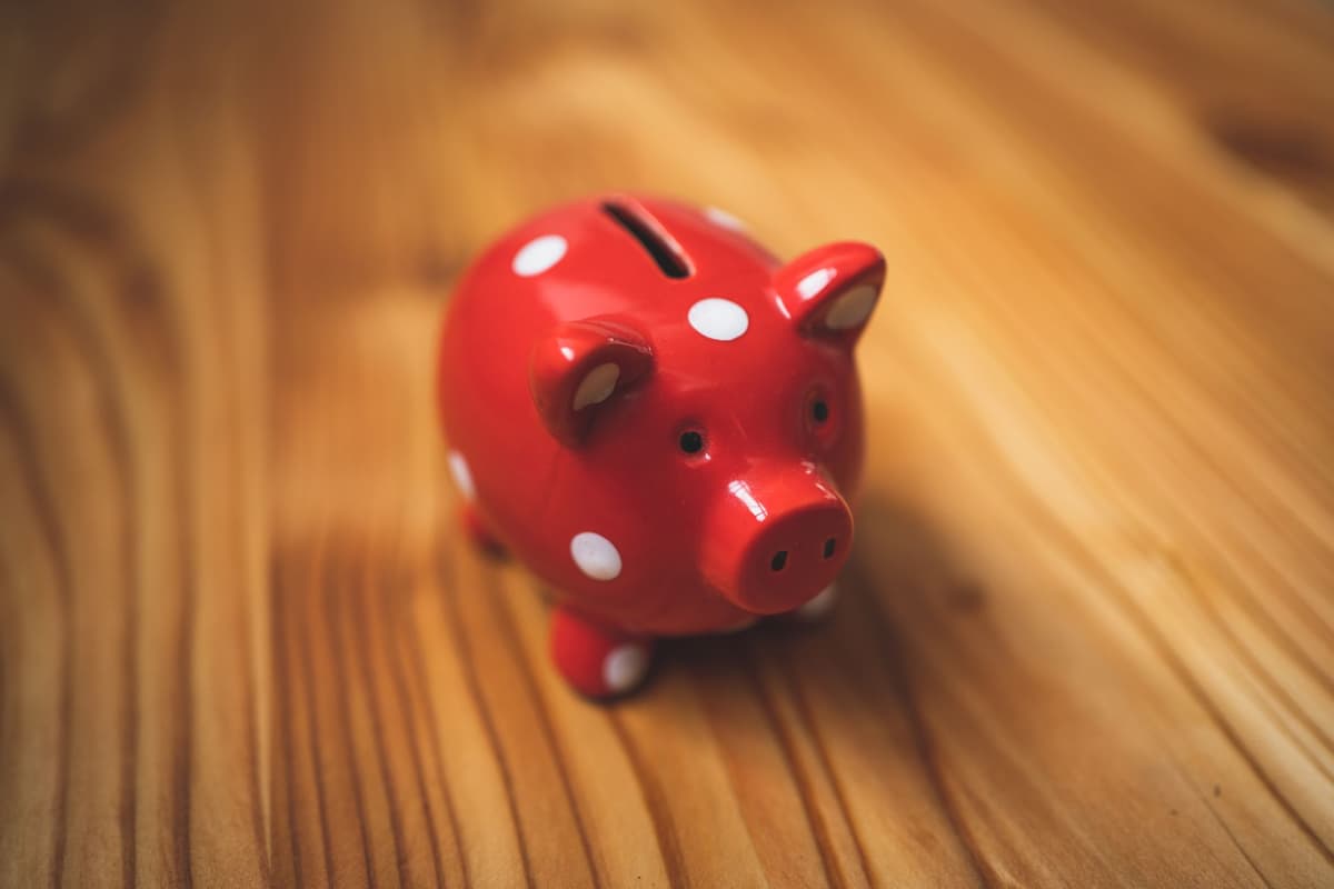 a person in a suit nervously looking at a giant, oversized piggy bank with a tiny slot